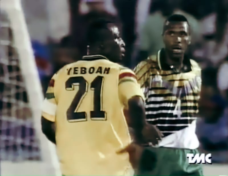 A screengrabbed image of Tony Yeboah in the foreground, with his back turned, so we can see the 'Yeboah 21' on back of his gold Ghana shirt, with Lucas Radebe to the right facing us, or more accurately facing Yeboah, keeping a close eye on his rival